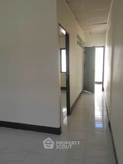 Bright hallway with tiled flooring leading to open door and natural light.