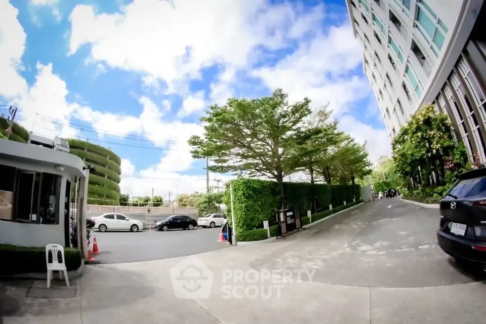Modern building exterior with lush greenery and driveway under a bright blue sky.