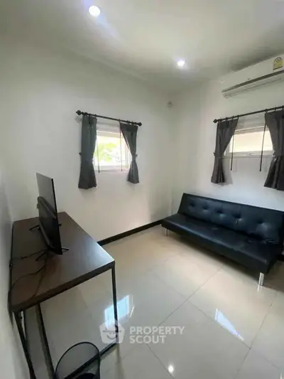 Modern minimalist living room with sleek black sofa and wall-mounted TV, perfect for cozy relaxation.