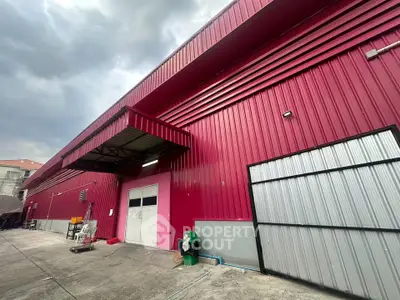 Vibrant red industrial warehouse exterior with large doors and overcast sky.