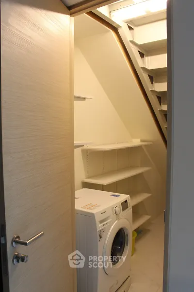 Compact laundry room with washing machine under staircase, featuring built-in shelves for storage.