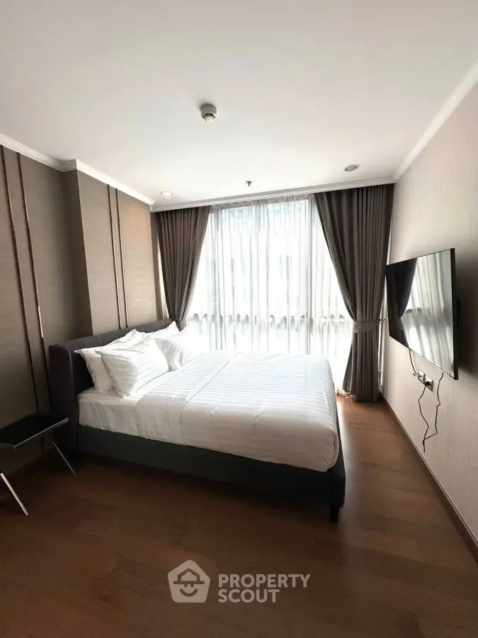 Modern bedroom with large window and wall-mounted TV in stylish apartment.