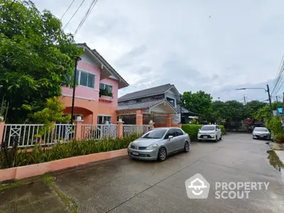 Charming suburban street view with colorful houses and parked cars, surrounded by lush greenery.