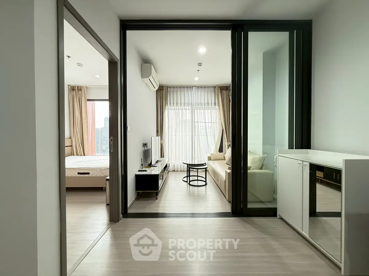 Modern apartment with open living room and bedroom, featuring sleek furniture and large windows.