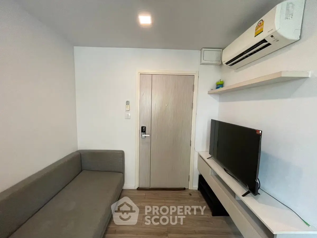 Modern living room with sleek sofa and wall-mounted TV, featuring minimalist design and air conditioning.