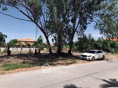 Vacant land with trees and a parked car on a sunny day.