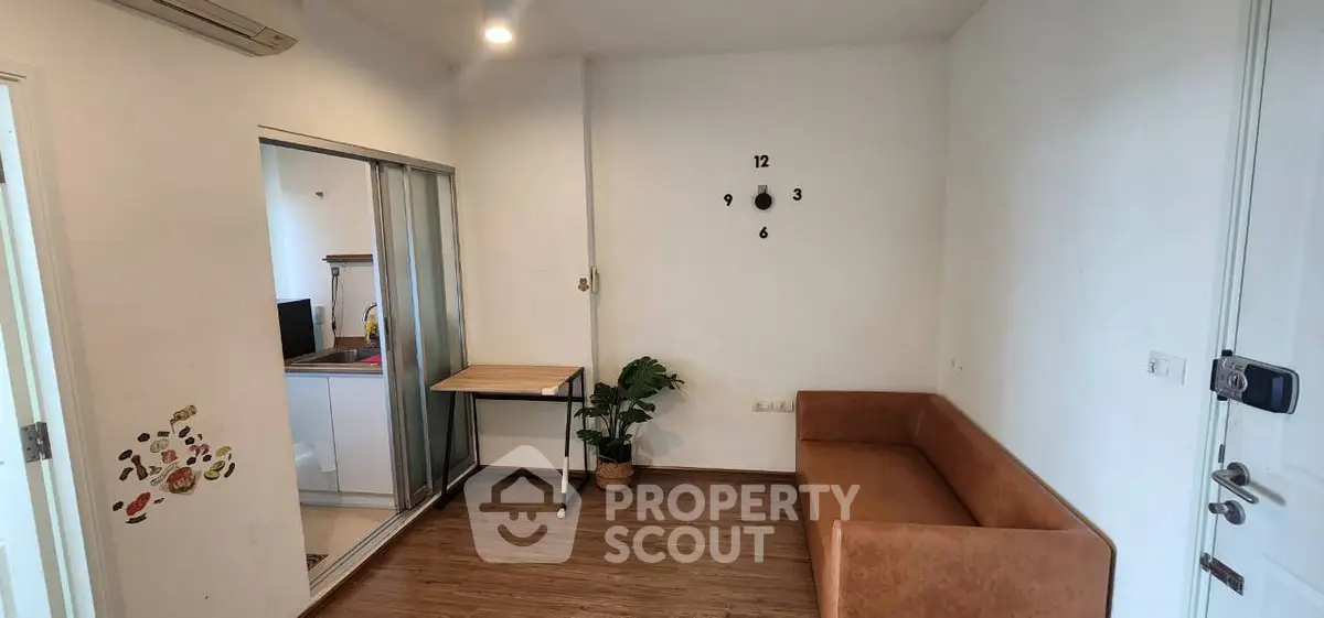 Cozy living room with modern decor and wooden flooring, featuring a stylish sofa and wall clock.