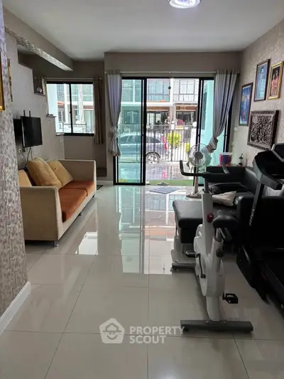 Spacious living room with modern decor and exercise equipment, featuring large windows for natural light.