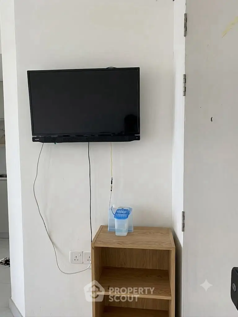 Modern apartment interior with wall-mounted TV and minimalist wooden shelf.