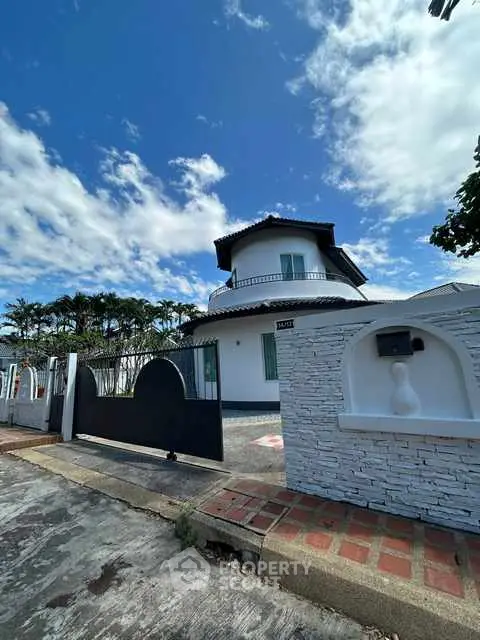 Charming white house with modern gate and lush greenery under a bright blue sky.