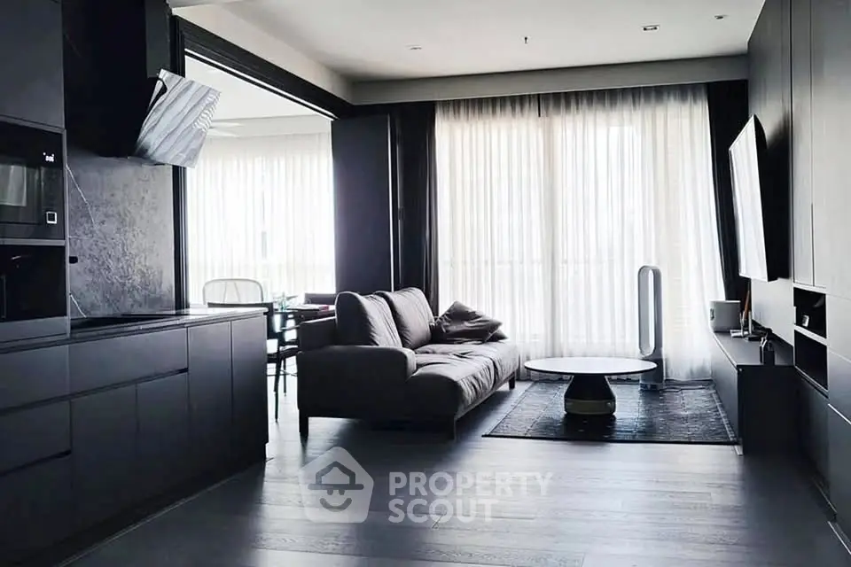 Modern living room with sleek black furniture and large windows offering natural light.