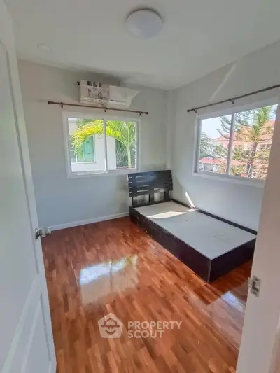 Bright bedroom with wooden flooring and large windows offering natural light and garden views.