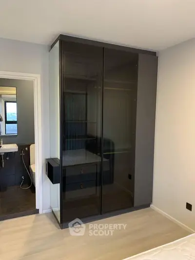 Modern bedroom with sleek black wardrobe and view into stylish bathroom