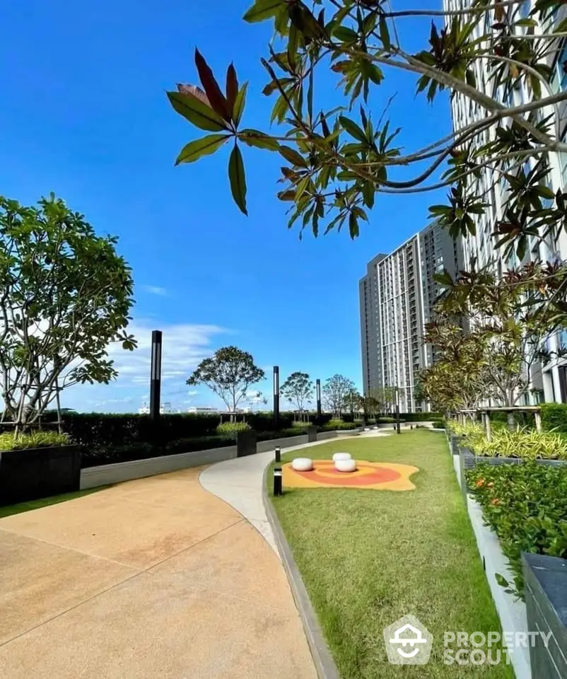 Modern high-rise building with landscaped garden and walking path under clear blue sky.