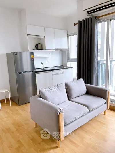 Modern apartment interior with cozy sofa and sleek kitchen area featuring stainless steel fridge and large windows.