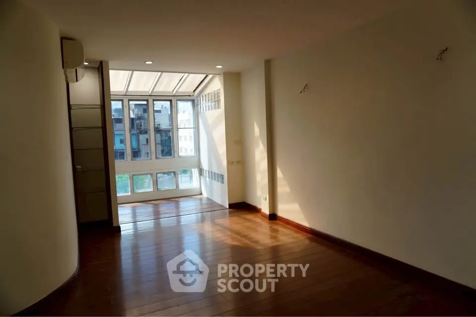 Spacious sunlit room with wooden flooring and large windows in modern apartment.