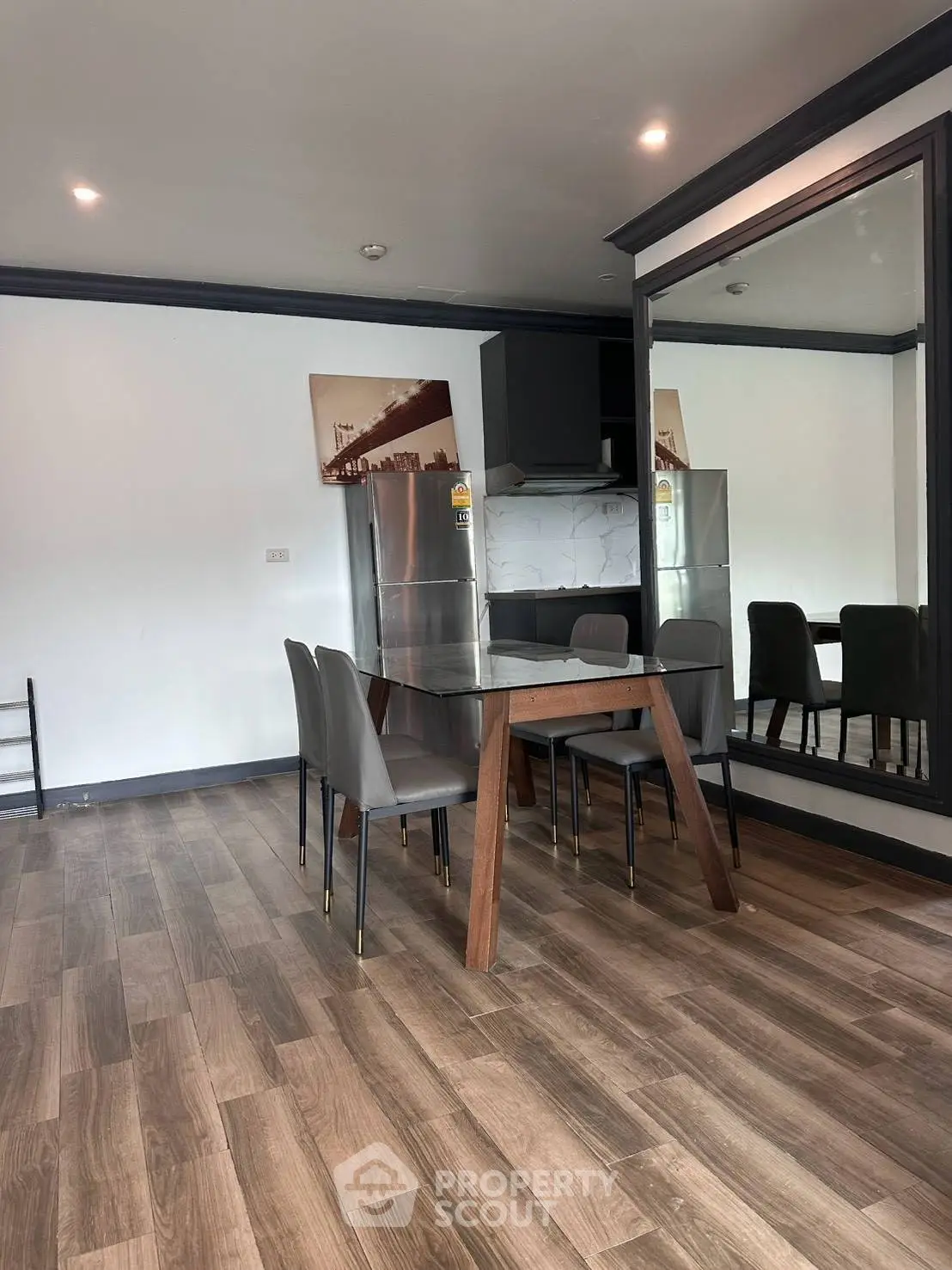 Modern dining area with sleek wooden table and chairs, adjacent to a stainless steel refrigerator and large mirror.