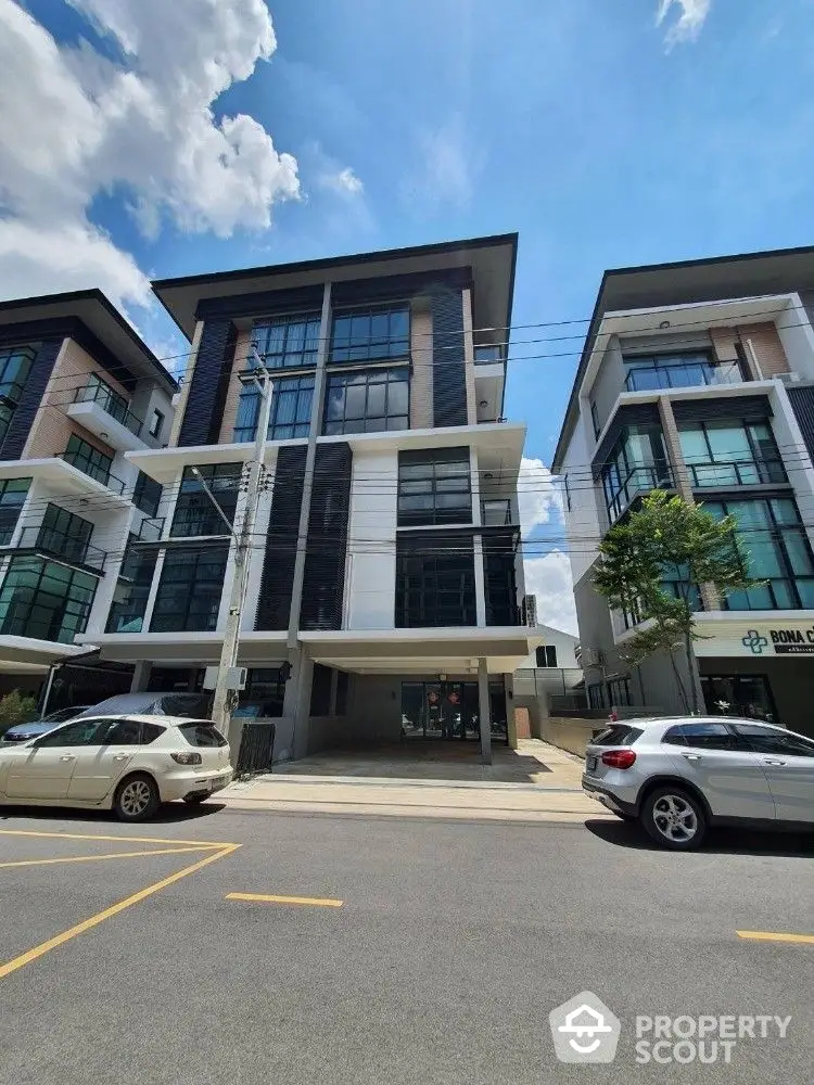 Modern commercial real estate featuring large glass windows, sleek design, and ample parking space under a clear blue sky.