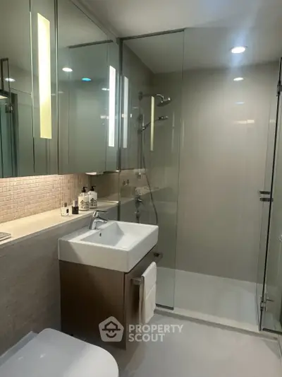 Modern bathroom with glass shower, sleek vanity, and ambient lighting