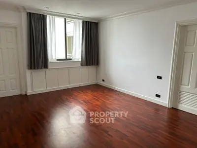 Spacious empty room with elegant wooden flooring and large window, perfect for customization.