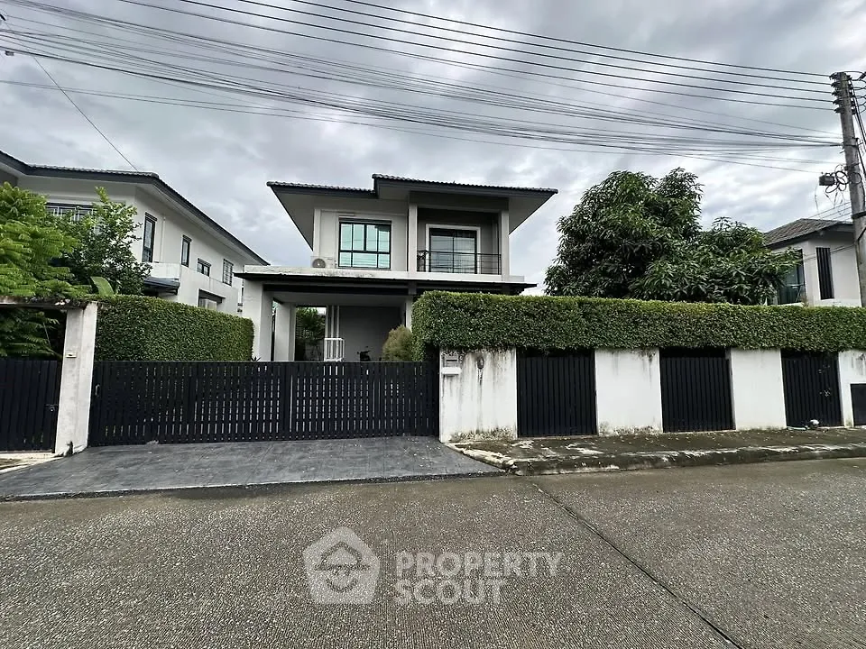 Modern two-story house with gated entrance and lush greenery in a suburban neighborhood.