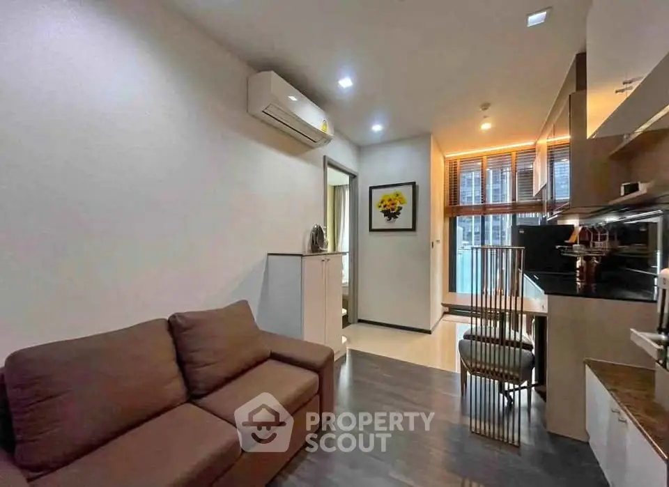 Modern living room with sleek design and open kitchen layout, featuring stylish furniture and bright lighting.