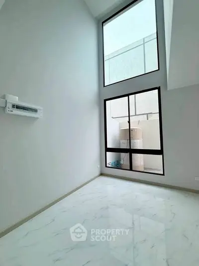 Spacious room with high ceiling and large windows, perfect for natural light.