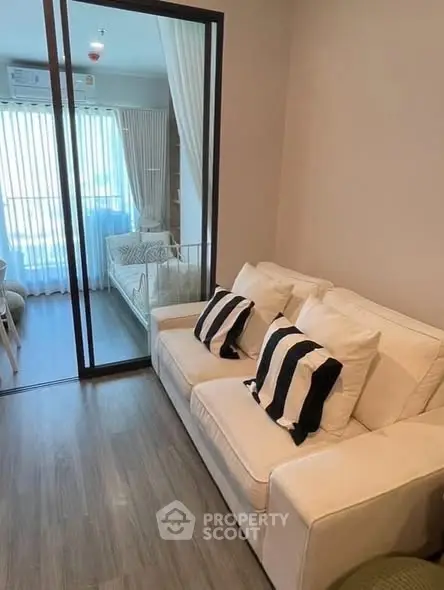 Cozy living room with modern decor and glass partition leading to a bright bedroom.