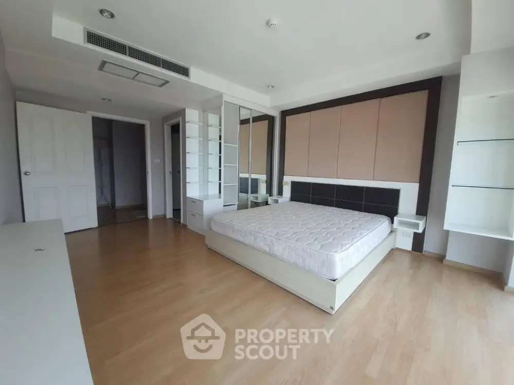 Spacious bedroom with modern design and ample natural light, featuring a stylish bed and sleek wooden flooring.