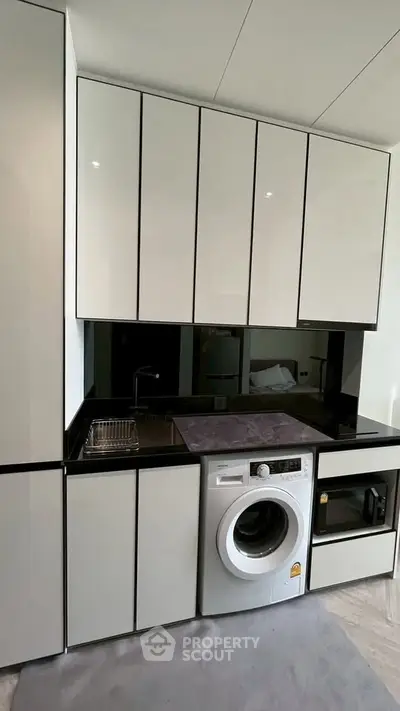 Modern compact kitchen with sleek cabinetry and built-in appliances, including washing machine and microwave.