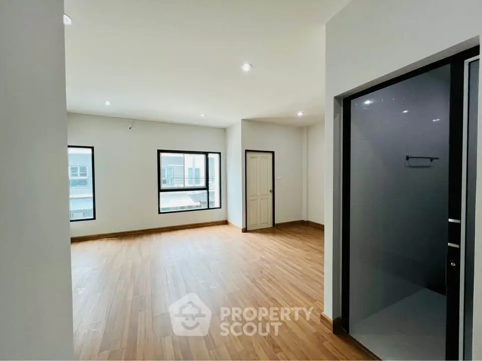 Spacious empty room with wooden flooring and large windows in modern apartment.