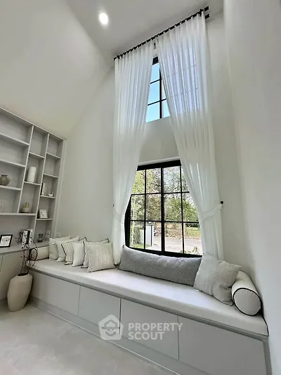 Elegant living room with high ceilings, large window, and cozy seating area with cushions.