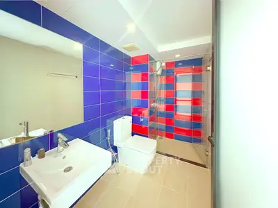 Modern bathroom with vibrant blue and red tiles, featuring a sleek sink and glass shower enclosure.