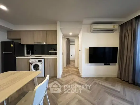 Modern open-plan living area with kitchen, washing machine, and wall-mounted TV.