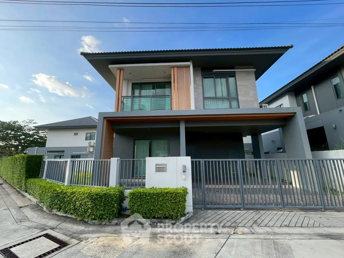 Modern two-story house with sleek design and gated entrance in a suburban neighborhood.