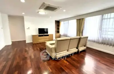 Spacious living room with hardwood floors and modern furnishings in a bright apartment.
