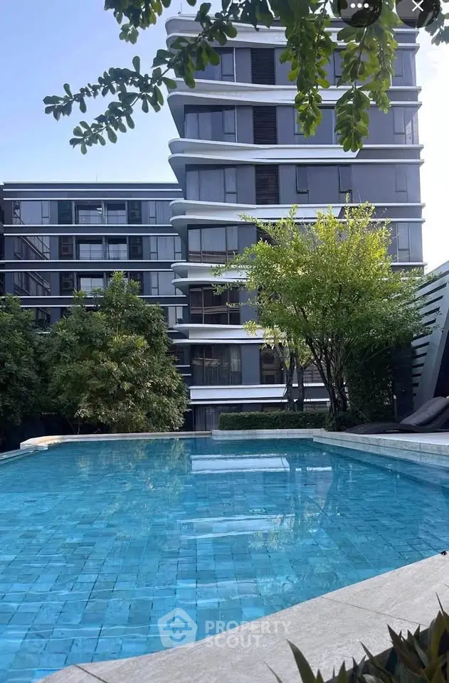 Modern apartment building with sleek design overlooking a serene swimming pool surrounded by lush greenery.