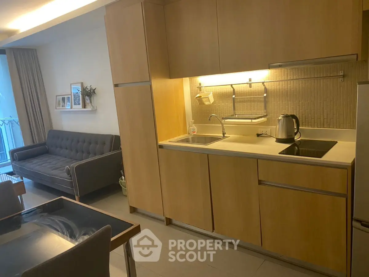 Modern kitchen with wooden cabinets and cozy living area in open layout apartment.