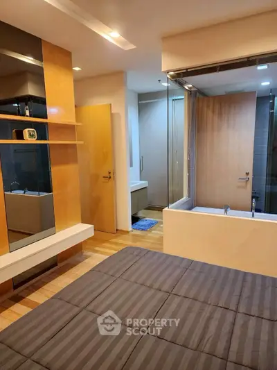 Modern bedroom with ensuite bathroom featuring glass partition and wooden accents.