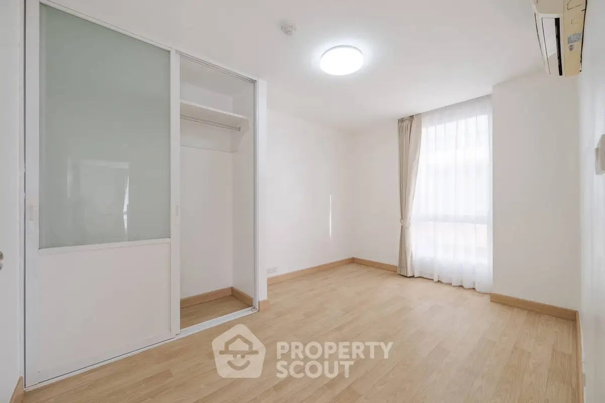 Spacious empty bedroom with wooden flooring and large window, perfect for customization.
