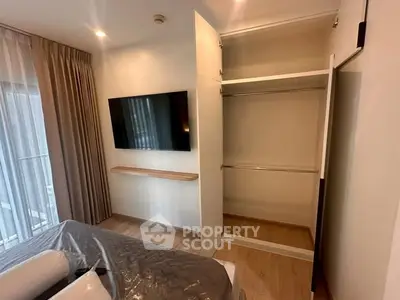 Modern bedroom with open closet and wall-mounted TV, featuring elegant curtains and wooden flooring.