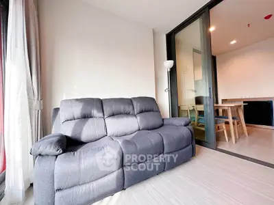 Modern living room with cozy gray sofa and dining area in open layout apartment.