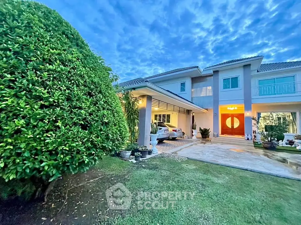 Luxurious two-story home with manicured garden and spacious driveway at dusk.