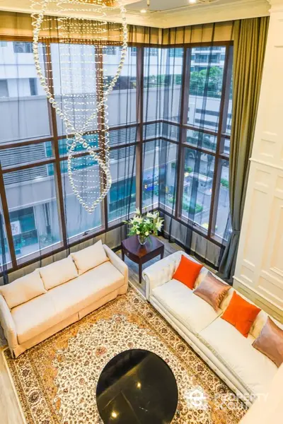 Luxurious high-ceiling living room with elegant chandelier and large windows offering city views.