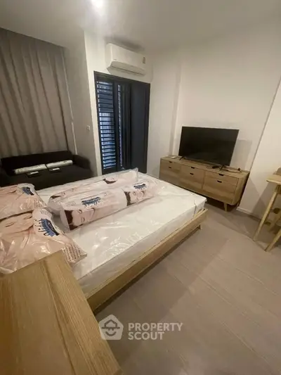 Modern bedroom with sleek furniture and natural light, featuring a cozy bed and stylish TV setup.