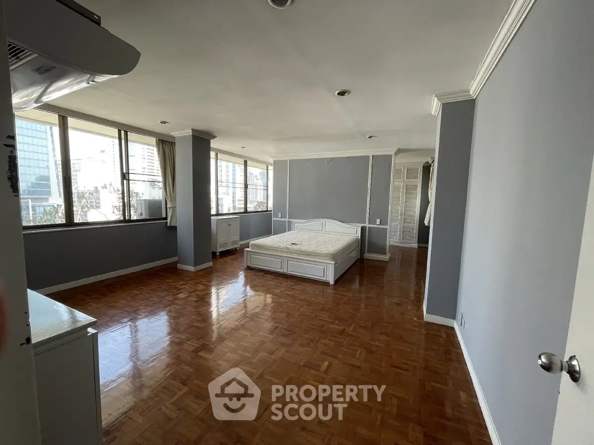 Spacious bedroom with large windows and wooden flooring in a modern apartment.