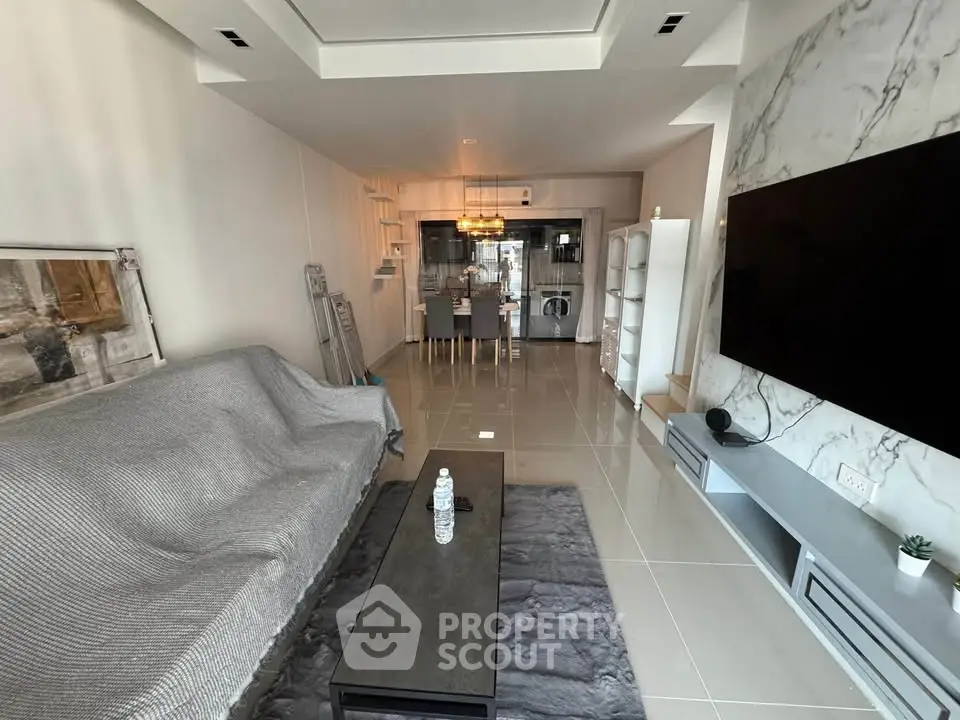 Modern living room with sleek design and open kitchen layout, featuring a large TV and stylish furniture.