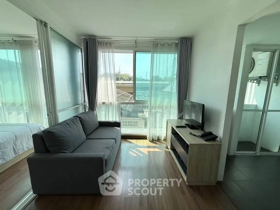 Modern living room with sleek sofa and TV, featuring large windows and abundant natural light.