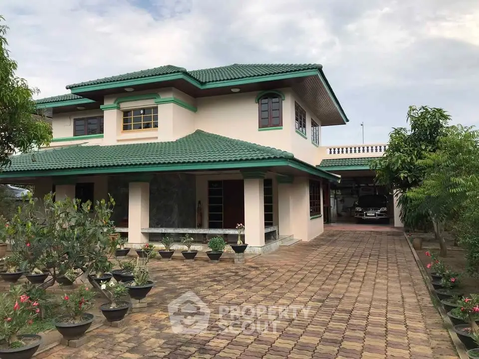 Charming two-story house with green roof and spacious driveway surrounded by lush garden.