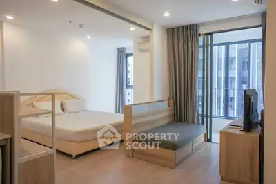 Modern studio apartment with bed, sofa, and large windows offering city views.
